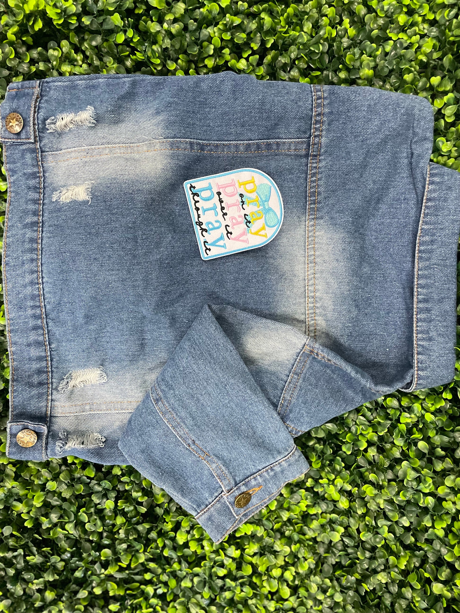 Embroidered patch with 'pray on it, pray over it, pray through it' text in various colors placed on a children's denim jean jacket