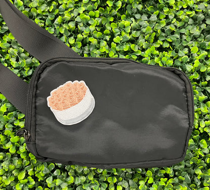 An embroidered patch in the shape of a bundle of roses with pink petals and green leaves, placed on a black shoulder bag against a green backdrop