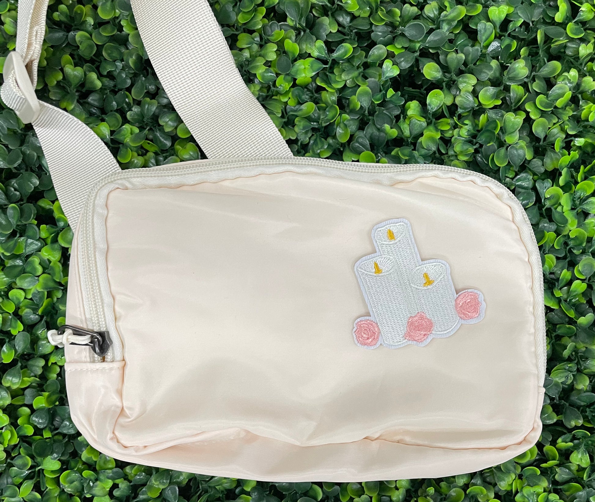 A patch with embroidered candles and roses in pink and yellow colors on a white background, placed on a white shoulder bag