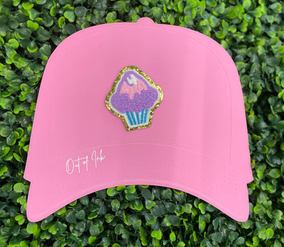 Decorative patch of a cupcake with pink and purple frosting, placed on a pink trucker hat graphic