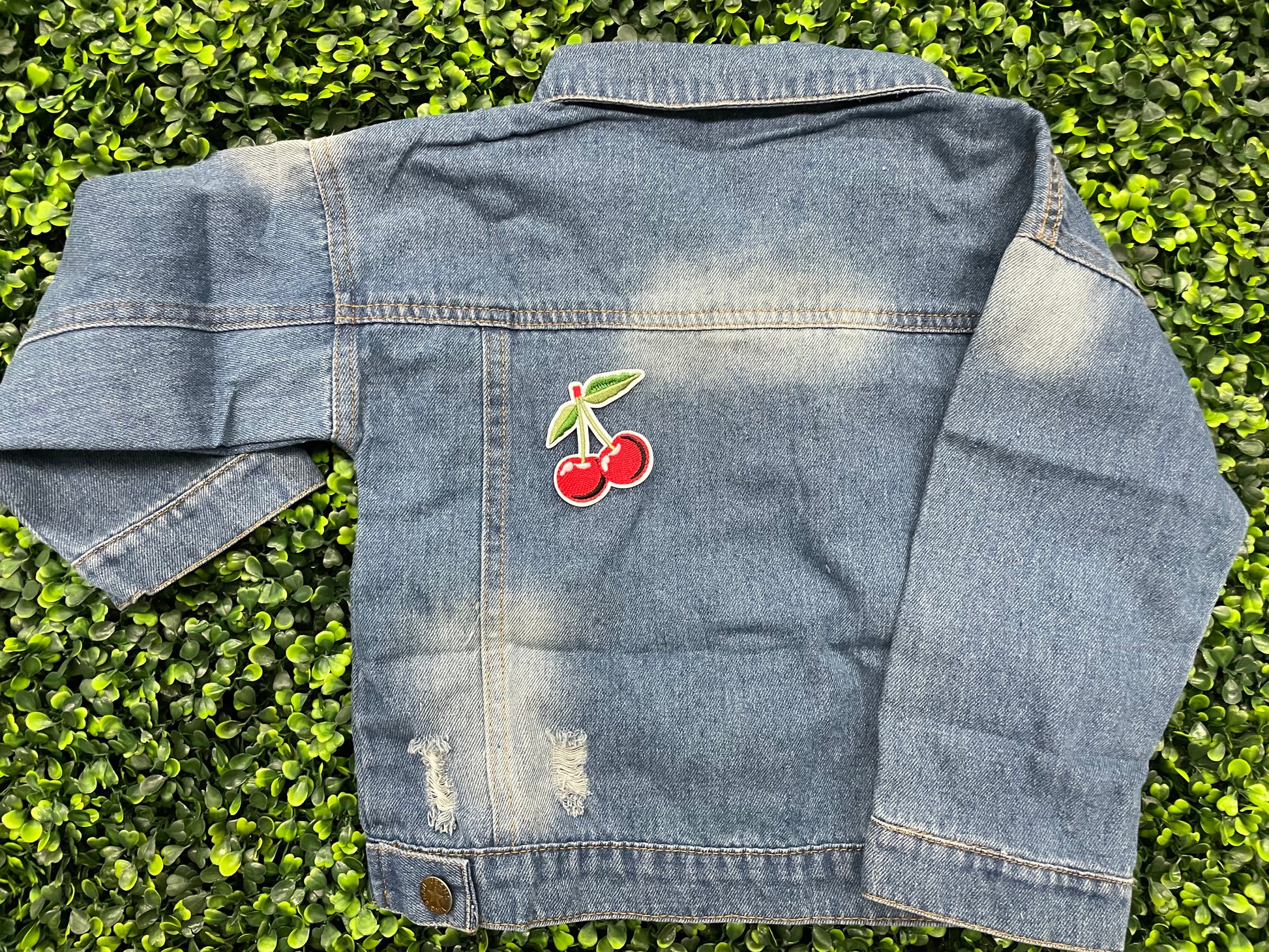 A patch with two red cherries and a green leaf embroidered on it, placed on a jean jacket