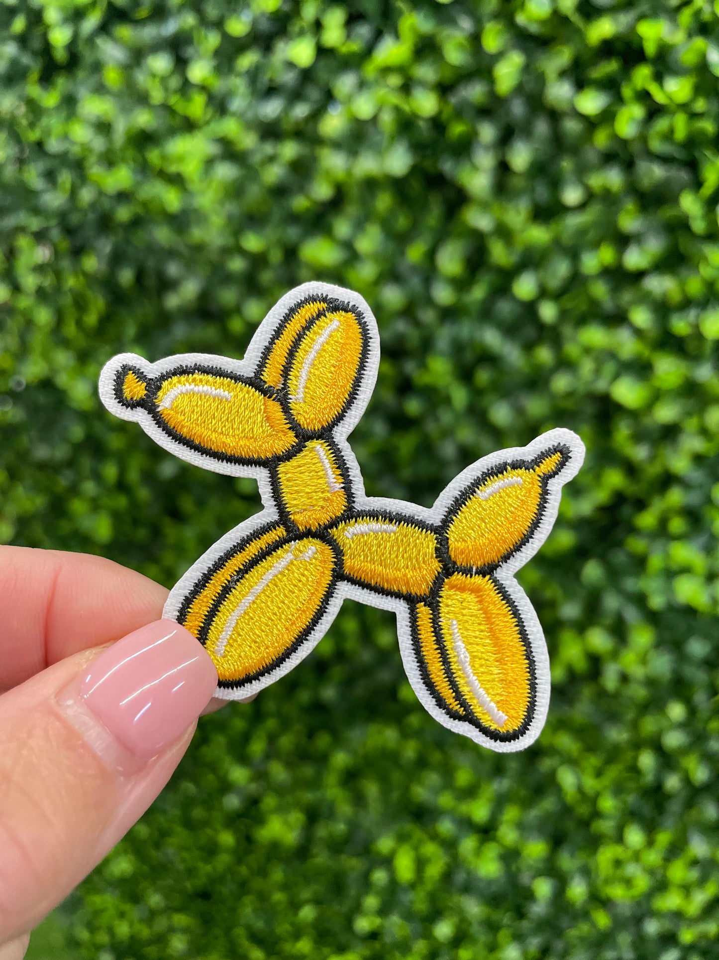 Yellow balloon dog-shaped patch in front of a green leafy background