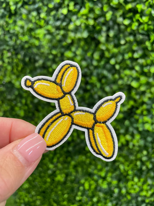 Yellow balloon dog-shaped patch in front of a green leafy background